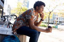 Африканский американец сидит в городе и пользуется смартфоном. цифровая реклама на ходу, на улице и по городу. — стоковое фото