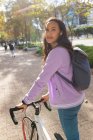 Портрет улыбающейся азиатки, катающейся на велосипеде и смотрящей в камеру в солнечном парке. независимая молодая женщина в городе. — стоковое фото