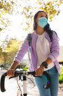 Mulher asiática usando máscara facial bicicleta de rodas no parque ensolarado. jovem independente para fora e sobre na cidade durante coronavírus covid 19 pandemia. — Fotografia de Stock
