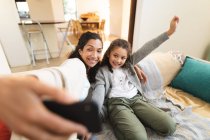 Mestiço mãe e filha sentados no sofá fazendo caras engraçadas, tirando selfie. estilo de vida doméstico e passar tempo de qualidade em casa. — Fotografia de Stock