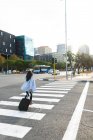 Asiatin überquert Straße mit Koffer. Unabhängige junge Frau in der Stadt unterwegs. — Stockfoto