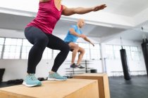 Белый мужчина и женщина тренируются в спортзале, прыгают на коробках. силовые и фитнес-кросс тренировки для бокса. — стоковое фото