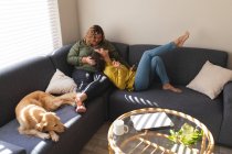 Счастливая лесбийская пара обнимается и сидит на диване с собакой. бытовой образ жизни, свободное время дома. — стоковое фото