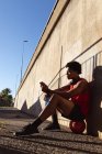 Ajuste hombre afroamericano haciendo ejercicio en la ciudad con el teléfono inteligente en la calle. fitness y estilo de vida urbano activo al aire libre. - foto de stock