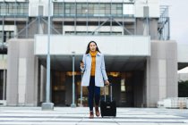 Asian woman holding smartphone and walking with suitcase in the street. independent young woman out and about in the city. — Stock Photo