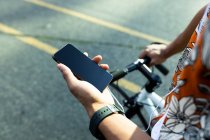 Hombre en la ciudad sentado en bicicleta y utilizando el teléfono inteligente. nómada digital sobre la marcha, fuera y alrededor de la ciudad. - foto de stock