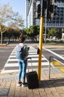 Asiatin überquert Straße mit Koffer und hält Kaffee zum Mitnehmen Unabhängige junge Frau in der Stadt unterwegs. — Stockfoto