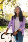 Mujer asiática sonriente rodando bicicleta en el soleado parque. mujer joven independiente fuera y alrededor de la ciudad. - foto de stock