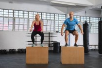 Homem e mulher caucasianos se exercitando no ginásio, pulando em caixas. treinamento cruzado de força e aptidão para boxe. — Fotografia de Stock