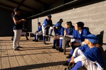 Groupe diversifié de joueuses de baseball assises sur le banc, à l'écoute de l'entraîneur féminin avant le match. équipe féminine de baseball, entraînement sportif et tactiques de jeu. — Photo de stock