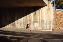 Ajuste hombre afroamericano ejerciendo en la ciudad corriendo en la calle. fitness y estilo de vida urbano activo al aire libre. - foto de stock
