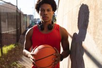 Retrato del hombre afroamericano en forma ejerciendo en la ciudad sosteniendo baloncesto en la calle. fitness y estilo de vida urbano activo al aire libre. - foto de stock