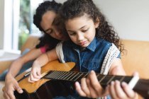 Мать и дочь смешанной расы сидят на диване и играют на гитаре. домашний образ жизни и проводить время дома. — стоковое фото
