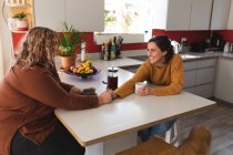 Lesbian couple smiling and drinking coffee in kitchen. domestic lifestyle, spending free time at home. — Stock Photo