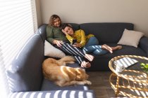Счастливая лесбийская пара обнимается и сидит на диване с собакой. бытовой образ жизни, свободное время дома. — стоковое фото