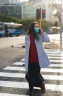 Asiatin trägt Gesichtsmaske und überquert Straße mit Koffer. Unabhängige junge Frau während der Coronavirus-Pandemie 19 in der Stadt unterwegs. — Stockfoto