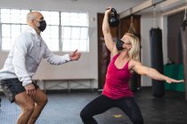 Кавказский тренер инструктирует женщину, которая занимается спортом в масках для лица, поднимает тяжести. силовые и фитнес-кросс тренировки для бокса во время пандемии коронавируса. — стоковое фото