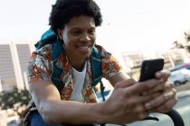 Африканский американец в городе сидит на велосипеде и пользуется смартфоном. цифровая реклама на ходу, на улице и по городу. — стоковое фото