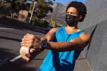 Fit afrikanisch-amerikanischer Mann, der in der Stadt mit Gesichtsmaske trainiert und sich auf der Straße dehnt. Fitness und aktiver urbaner Outdoor-Lebensstil während der Coronavirus-Pandemie 19. — Stockfoto