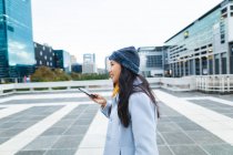 Mujer asiática sonriendo y usando smartphone en la calle. mujer joven independiente fuera y alrededor de la ciudad. - foto de stock