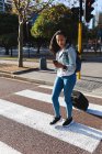 Asiatin überquert Straße mit Koffer und Smartphone Unabhängige junge Frau in der Stadt unterwegs. — Stockfoto