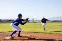 Смешанная раса женщина бейсболистка на солнечном бейсбольном поле тянется, чтобы поймать мяч во время игры. женская бейсбольная команда, спортивная подготовка и тактика игры. — стоковое фото