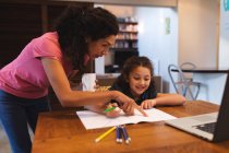 Madre di razza mista che tiene il caffè, aiutando sua figlia a fare i compiti. stile di vita domestico e trascorrere del tempo di qualità a casa. — Foto stock