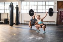 Entraîneur masculin caucasien instruisant la femme faisant de l'exercice au gymnase, soulevant des poids. musculation et fitness cross training pour la boxe. — Photo de stock