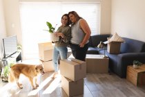 Lesbisches Paar mit Hund lächelt und umarmt sich beim Umzug. häuslicher Lebensstil, Freizeit zu Hause verbringen. — Stockfoto