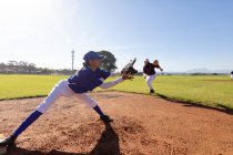 Mixed race female baseball player on sunny baseball field reaching to catch ball during game. female baseball team, sports training and game tactics. — Stock Photo