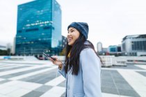 Азиатка улыбается и пользуется смартфоном на улице. независимая молодая женщина в городе. — стоковое фото