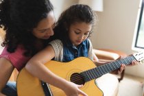 Mère et fille de race mixte assis sur le canapé et jouant de la guitare. style de vie domestique et passer du temps de qualité à la maison. — Photo de stock