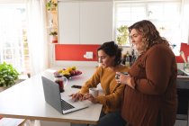Lesbisches Paar lächelt und benutzt Laptop in der Küche. häuslicher Lebensstil, Freizeit zu Hause verbringen. — Stockfoto