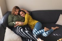 Счастливая лесбийская пара обнимается и сидит на диване. бытовой образ жизни, свободное время дома. — стоковое фото