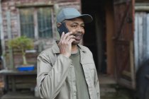 Jardineiro masculino afro-americano usando smartphone no centro de jardim. especialista que trabalha no viveiro de plantas bonsai, negócio de horticultura independente. — Fotografia de Stock