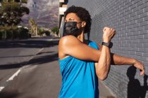 Подходящий африканский американец, тренирующийся в городе в маске для лица, растянувшийся на улице. фитнес и активный городской уличный образ жизни во время пандемии коронавируса. — стоковое фото