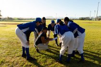 Diverse group of female baseball players standing in huddle around squatting coach on field. female baseball team, sports training and game tactics. — Stock Photo