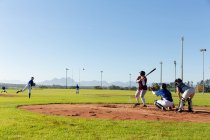 Groupe diversifié de joueuses de baseball en action sur un terrain de baseball ensoleillé pendant le match. équipe féminine de baseball, entraînement sportif et tactiques de jeu. — Photo de stock