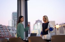 Two diverse female business colleagues talking and using laptop. working in business at a modern office. — Stock Photo