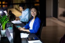 Retrato de una mujer de negocios asiática que trabaja de noche con auriculares. trabajar hasta tarde en los negocios en una oficina moderna. - foto de stock