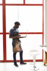 Afrikanischer Maler mit Gesichtsmaske und Laptop im Kunstatelier. Kreation und Inspiration in einem Malatelier während der Coronavirus-Pandemie 19. — Stockfoto