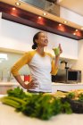 Mulher de raça mista sorridente na cozinha bebendo bebida saudável. estilo de vida doméstico, desfrutando de tempo de lazer em casa. — Fotografia de Stock