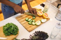 Mulher afro-americana na cozinha cortando legumes e frutas. estilo de vida doméstico, desfrutando de tempo de lazer em casa. — Fotografia de Stock