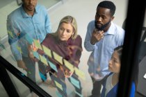 Diversi colleghi uomini e donne d'affari che leggono appunti colorati sulla parete di vetro. lavorare in azienda in un ufficio moderno. — Foto stock