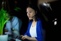 Mulher de negócios asiática trabalhando à noite usando fone de ouvido. trabalhando até tarde em negócios em um escritório moderno. — Fotografia de Stock
