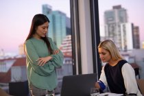 Two diverse female business colleagues talking and using laptop. working in business at a modern office. — Stock Photo
