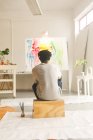 Pintor afroamericano en el trabajo mirando obras de arte en el estudio de arte. creación e inspiración en un estudio de pintura de artistas. - foto de stock