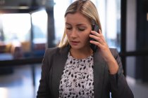 Kaukasische Geschäftsfrau im Smartphone-Gespräch und in grauer Jacke. Arbeit in einem modernen Büro. — Stockfoto