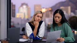 Dos compañeras de negocios diversas hablando y sosteniendo documentos. trabajar en un negocio en una oficina moderna. - foto de stock