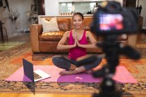 Lächelnde Mischlingshündin im Wohnzimmer, die Yoga-Vlog mit Laptop und Kamera macht. häuslicher Lebensstil, Freizeit zu Hause genießen. — Stockfoto